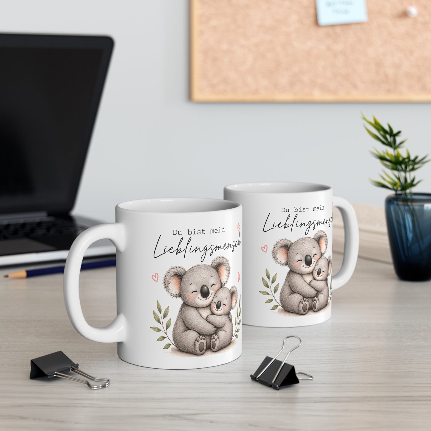 Zwei weiße Keramiktassen mit Koala-Motiv und dem Spruch „Du bist mein Lieblingsmensch“ auf einem Schreibtisch neben Laptop und Pflanze