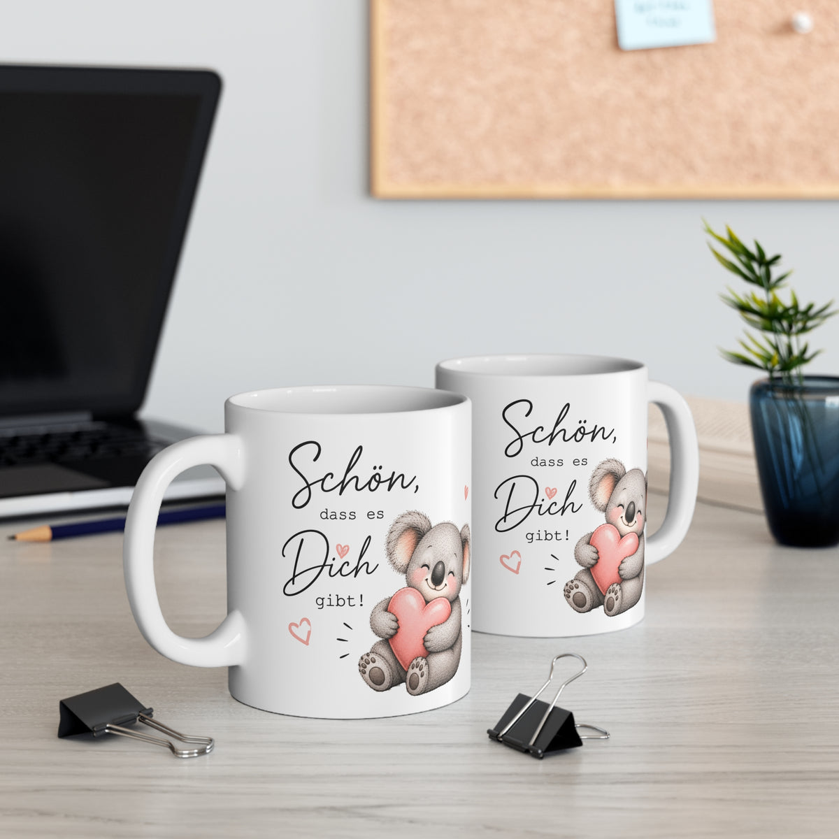 Zwei weiße Keramiktassen mit süßem Koala-Motiv und dem Spruch „Schön, dass es Dich gibt!“ auf einem Schreibtisch neben Laptop und Pflanze