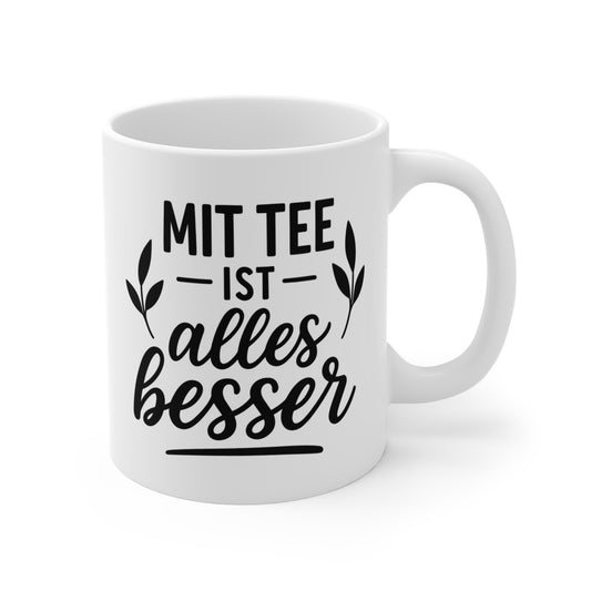 Weiße Tasse mit dem Schriftzug „Mit Tee ist alles besser“ und dekorativen Blättern