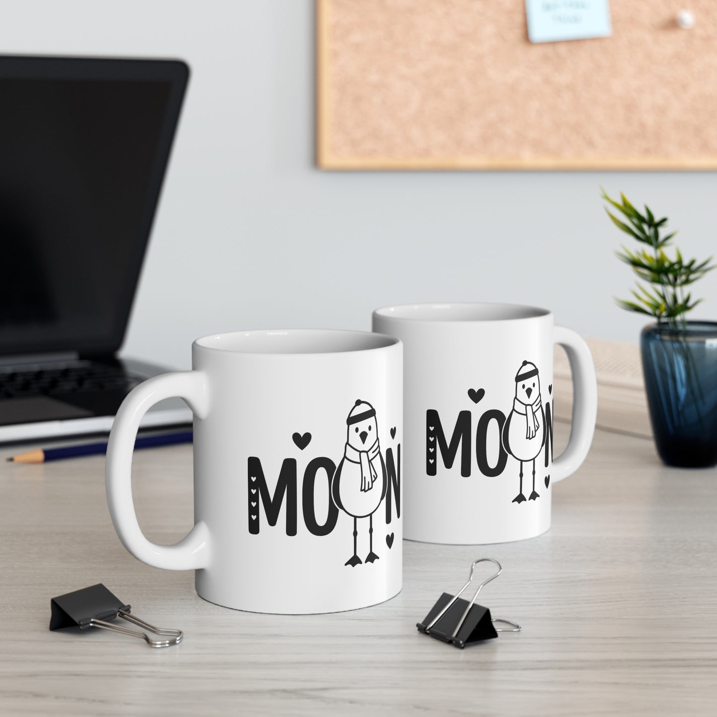 Zwei weiße Keramiktassen mit Moin Schriftzug und niedlicher Möwe auf einem Schreibtisch neben Laptop und Pflanze