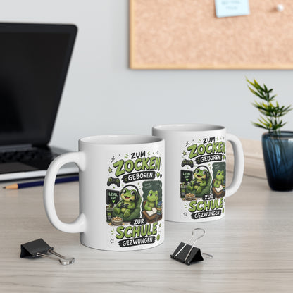 Zwei weiße Keramiktassen mit lustigem Frosch Gamer Motiv und Spruch „Zum Zocken geboren zur Schule gezwungen“ auf Schreibtisch