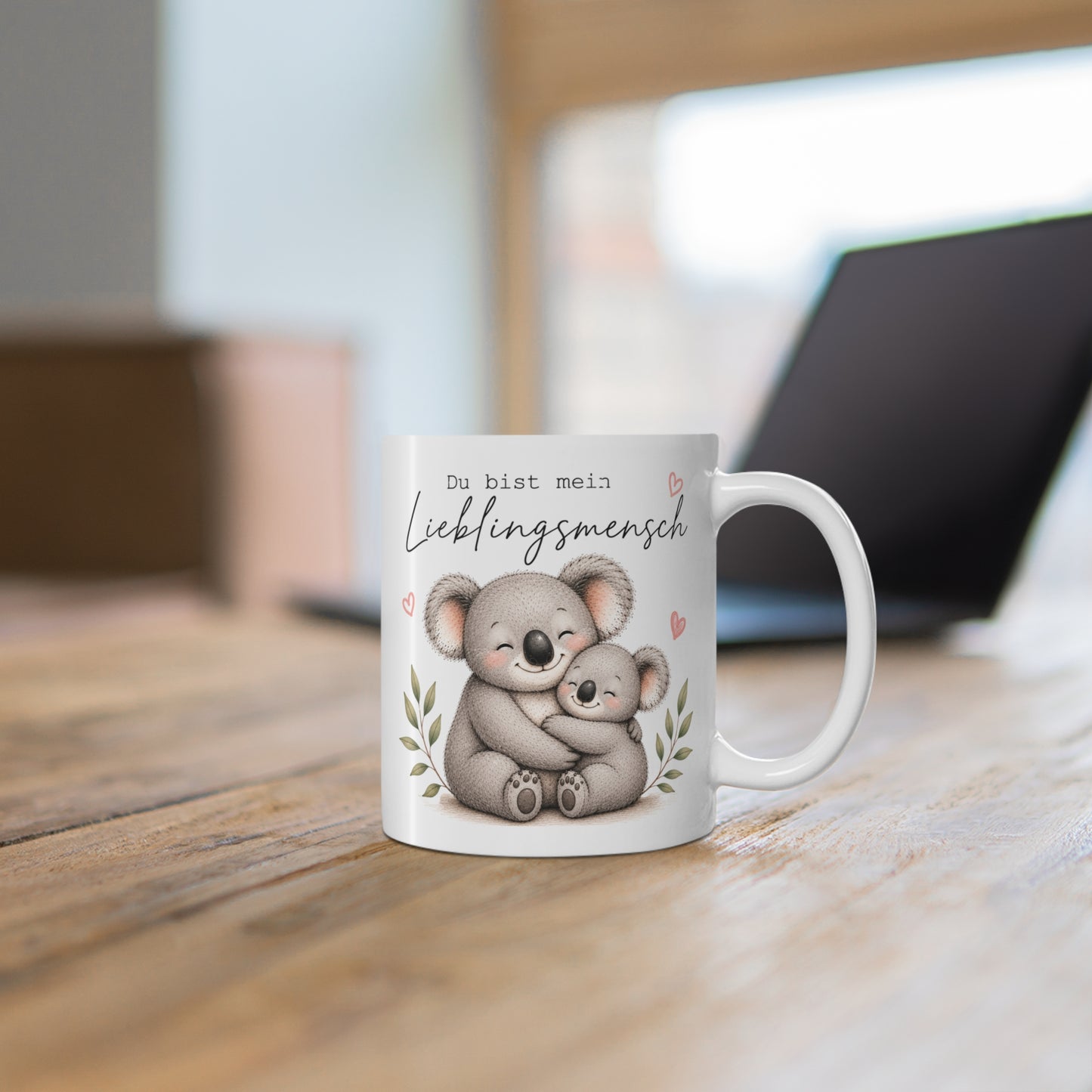 Weiße Tasse mit zwei liebevoll umarmenden Koalas und dem Schriftzug „Du bist mein Lieblingsmensch“ auf einem Holztisch