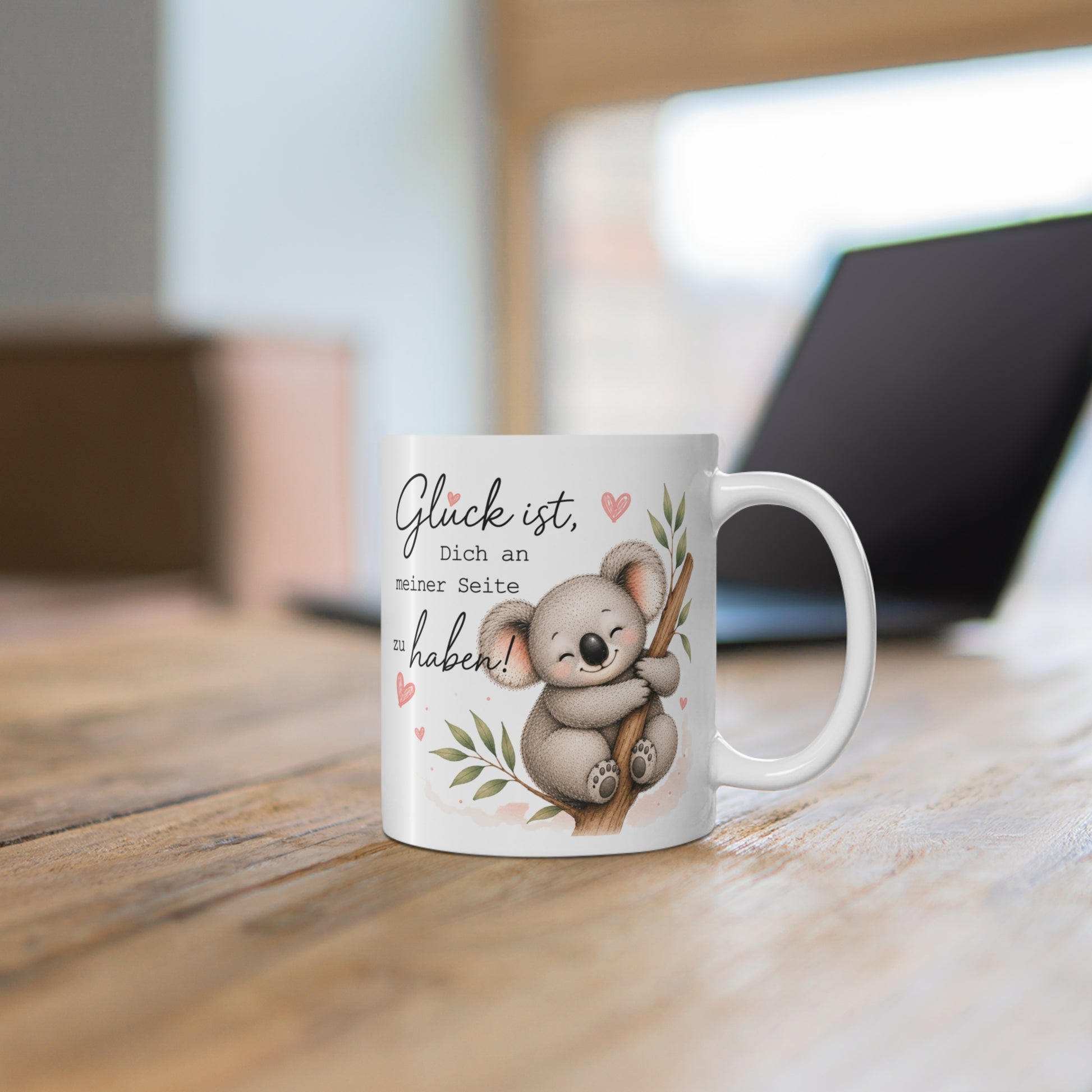 Weiße Tasse mit süßem Koala auf einem Ast und liebevollem Schriftzug auf einem Holztisch