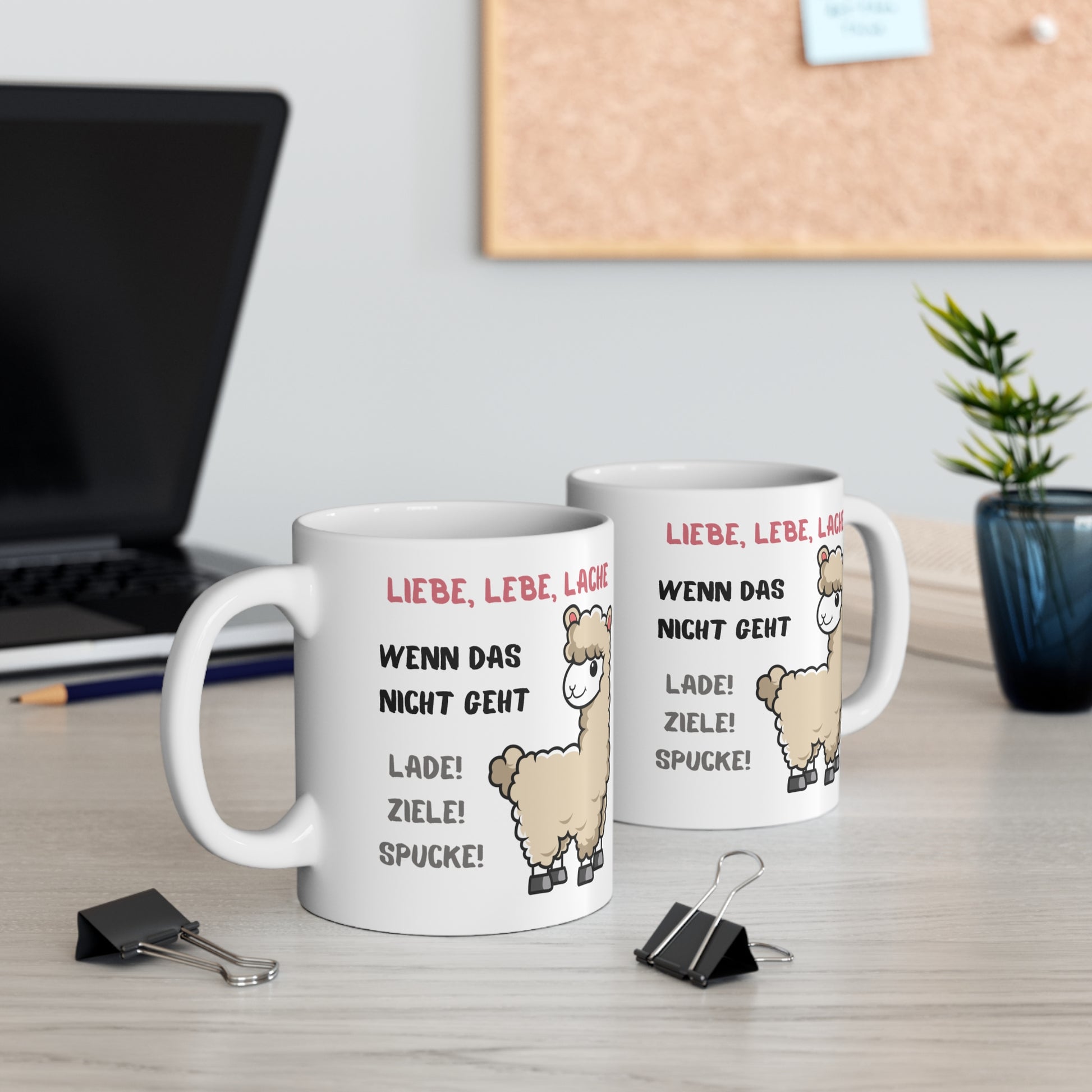Zwei weiße Keramiktassen mit lustigem Alpaka Motiv und Spruch auf einem Schreibtisch neben Laptop und Zimmerpflanze