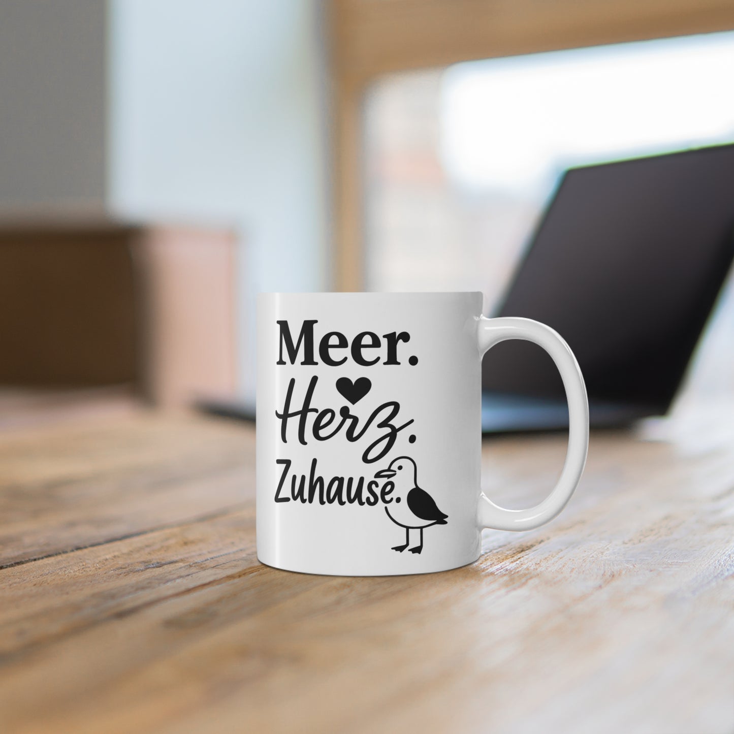 Weiße Tasse mit Küstenspruch „Meer. Herz. Zuhause.“ und kleiner Möwe auf einem Holztisch
