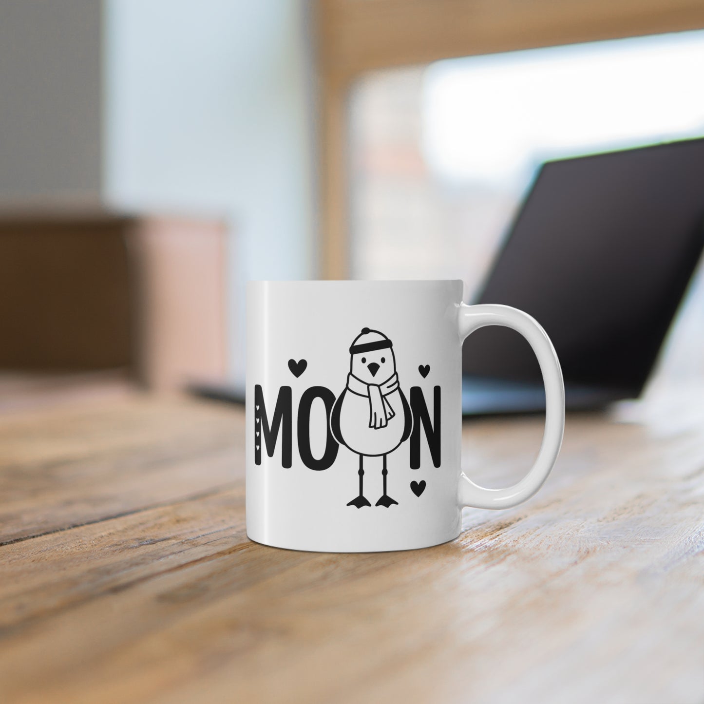 Weiße Keramiktasse mit Moin Motiv und winterlicher Möwe auf Holztisch vor unscharfem Hintergrund