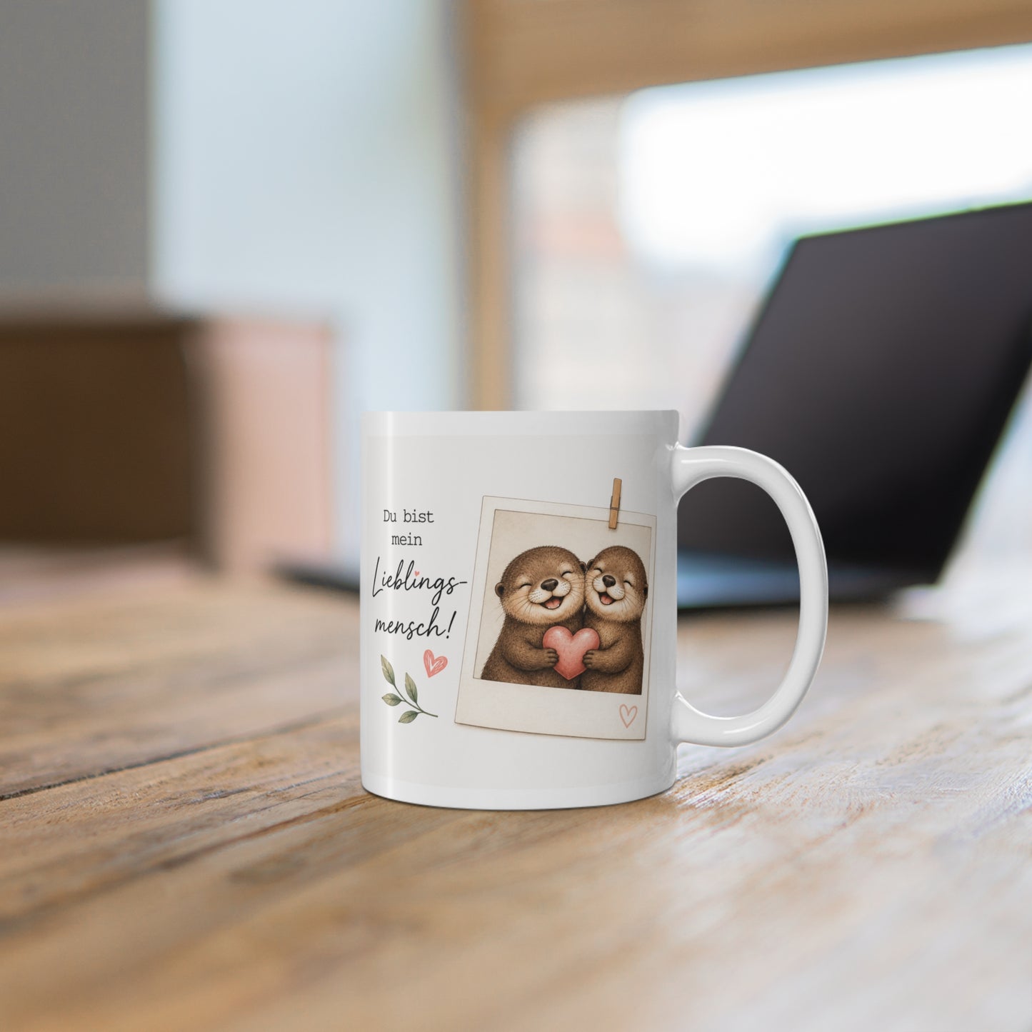 Weiße Tasse mit niedlichem Otterpaar im Polaroid-Stil und dem Spruch „Du bist mein Lieblingsmensch“ auf einem Holztisch