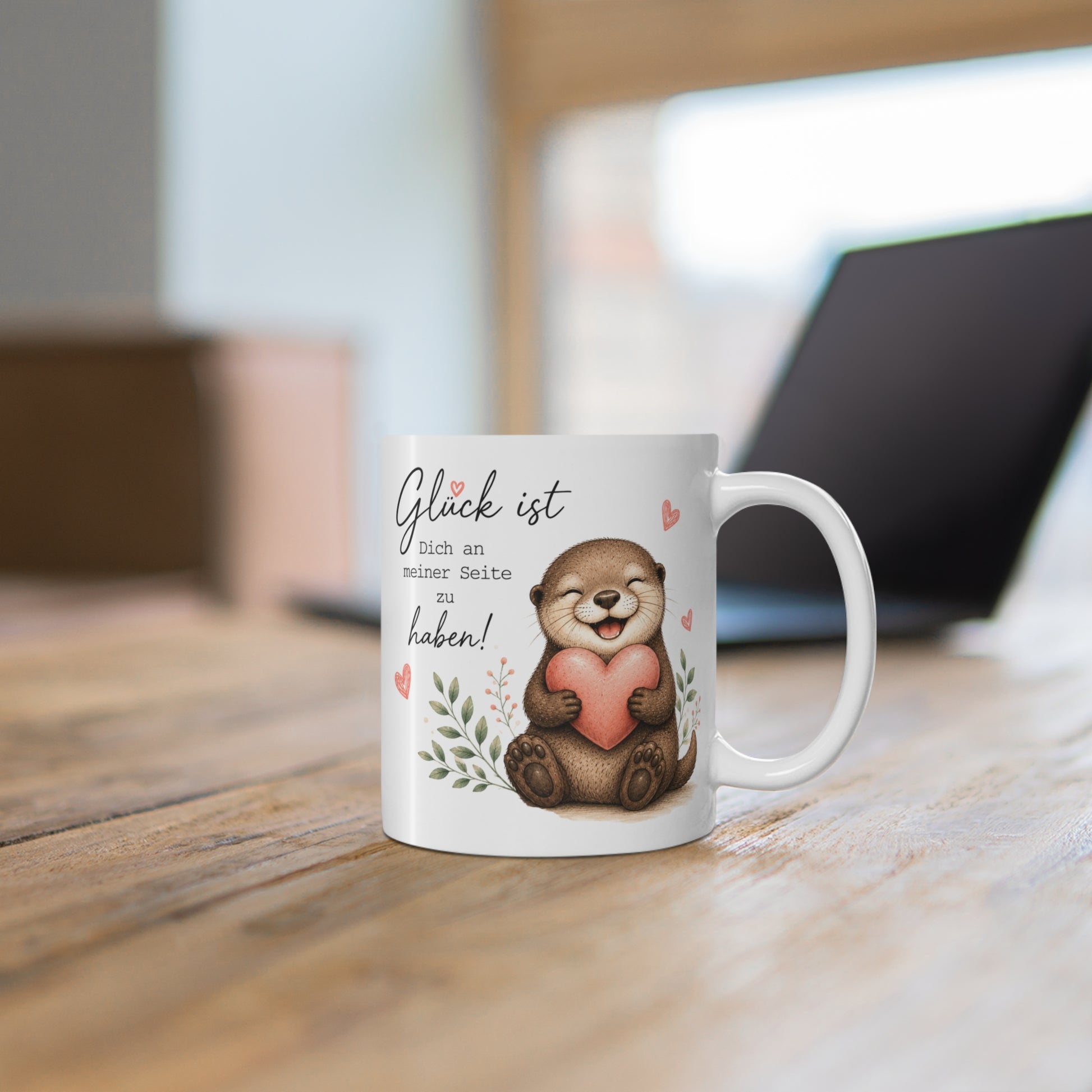 Weiße Tasse mit fröhlichem Otter, rosa Herz und dem Spruch „Glück ist Dich an meiner Seite zu haben“ auf einem Holztisch