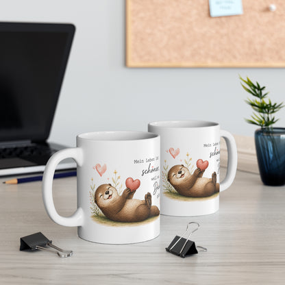 Zwei weiße Keramiktassen mit liegendem Otter, Herzmotiv und dem Spruch „Mein Leben ist schöner, weil es Dich gibt“ auf einem Schreibtisch