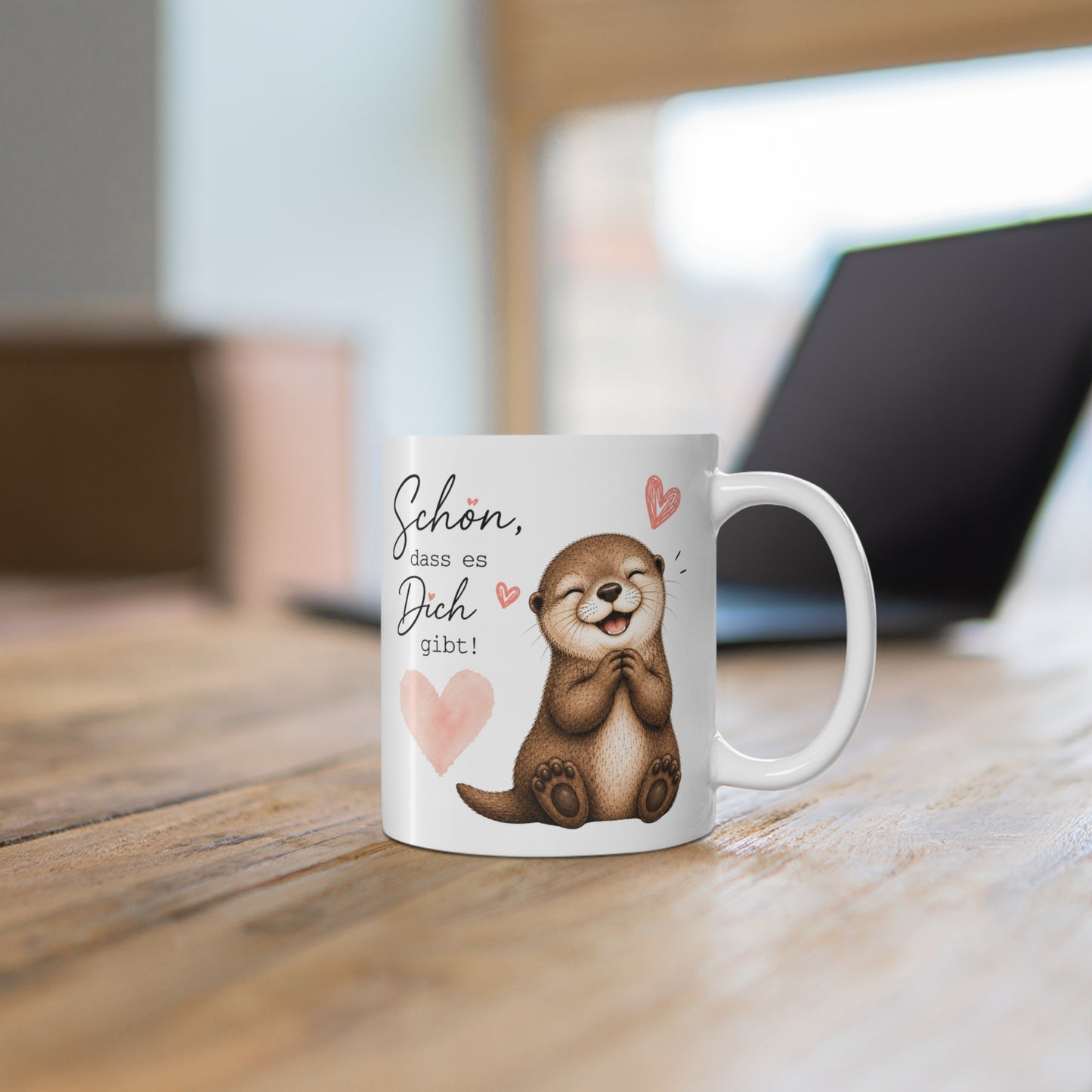 Weiße Tasse mit fröhlichem Otter, rosa Herz und dem liebevollen Spruch „Schön, dass es Dich gibt“ auf einem Holztisch