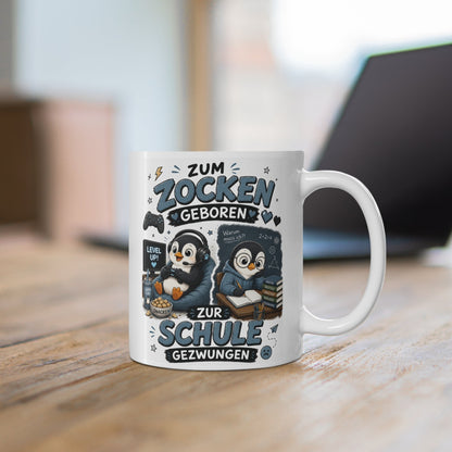 Weiße Keramiktasse mit niedlichem Pinguin Gamer Motiv und Spruch „Zum Zocken geboren zur Schule gezwungen“ auf Holztisch