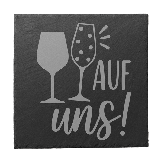 Quadratischer schwarzer Schiefer-Untersetzer mit Gravur „Auf uns!“ und Wein- sowie Sektglas Motiv