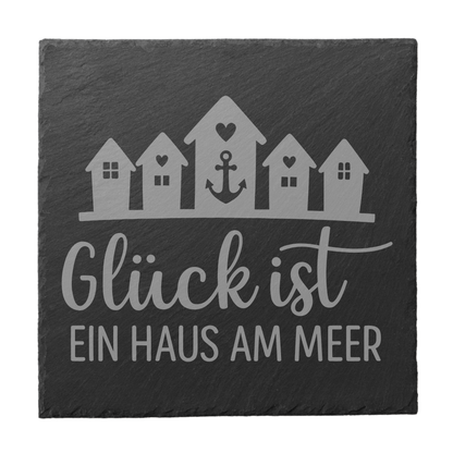 Quadratischer schwarzer Schiefer-Untersetzer mit Gravur „Glück ist ein Haus am Meer“ und Strandhäusern mit Anker
