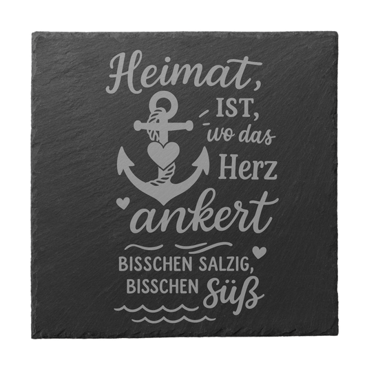 Quadratischer schwarzer Schiefer-Untersetzer mit Gravur „Heimat ist, wo das Herz ankert“ und Anker mit Herzdetail
