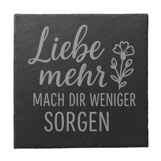 Quadratischer schwarzer Schiefer-Untersetzer mit Gravur „Liebe mehr, mach dir weniger Sorgen“ und floraler Illustration