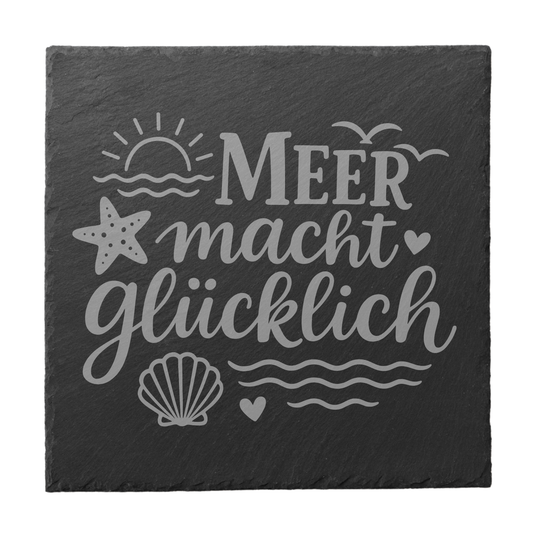 Quadratischer schwarzer Schiefer-Untersetzer mit Gravur „Meer macht glücklich“ sowie Sonne, Wellen, Seestern und Muschel