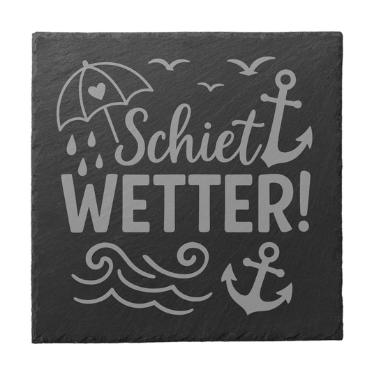 Quadratischer schwarzer Schiefer-Untersetzer mit Gravur „Schietwetter!“ und maritimen Symbolen wie Anker und Regenschirm