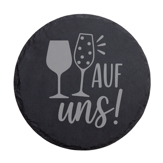 Runder schwarzer Schiefer-Untersetzer mit Schriftzug „Auf uns!“ und zwei Gläsern