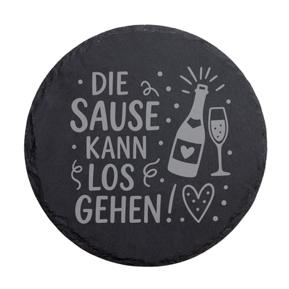 Runder schwarzer Schiefer-Untersetzer mit Spruch „Die Sause kann losgehen!“ und Sektglas Motiv