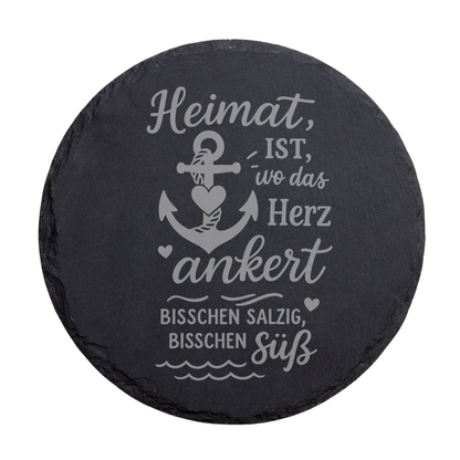 Runder schwarzer Schiefer-Untersetzer mit maritimem Spruch „Heimat ist wo das Herz ankert“ und dekorativem Anker