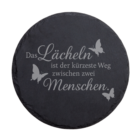 Runder schwarzer Schiefer-Untersetzer mit motivierendem Spruch „Das Lächeln ist der kürzeste Weg zwischen zwei Menschen“