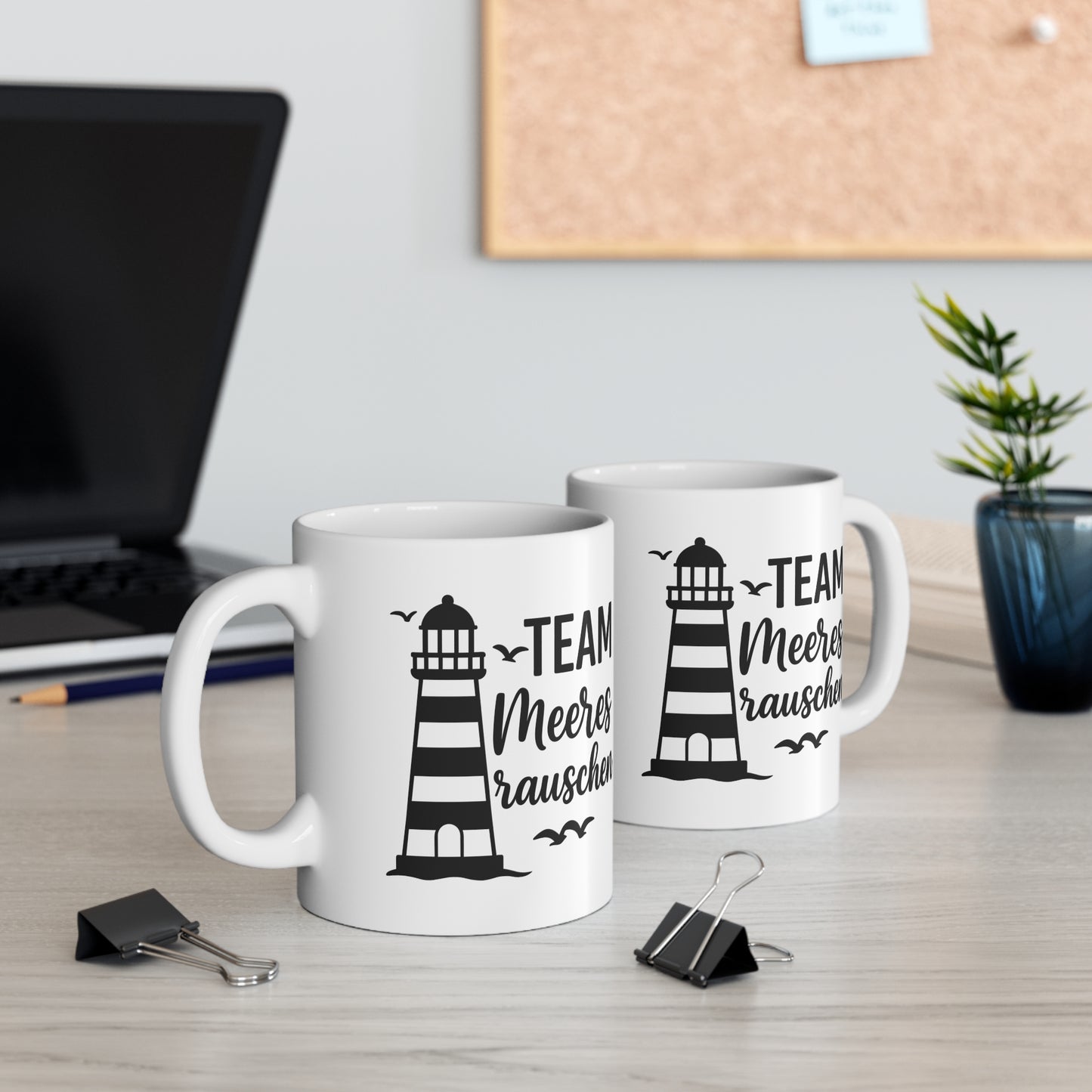 Zwei weiße Keramiktassen mit Leuchtturm-Motiv und dem Spruch „Team Meeresrauschen“ auf einem Schreibtisch