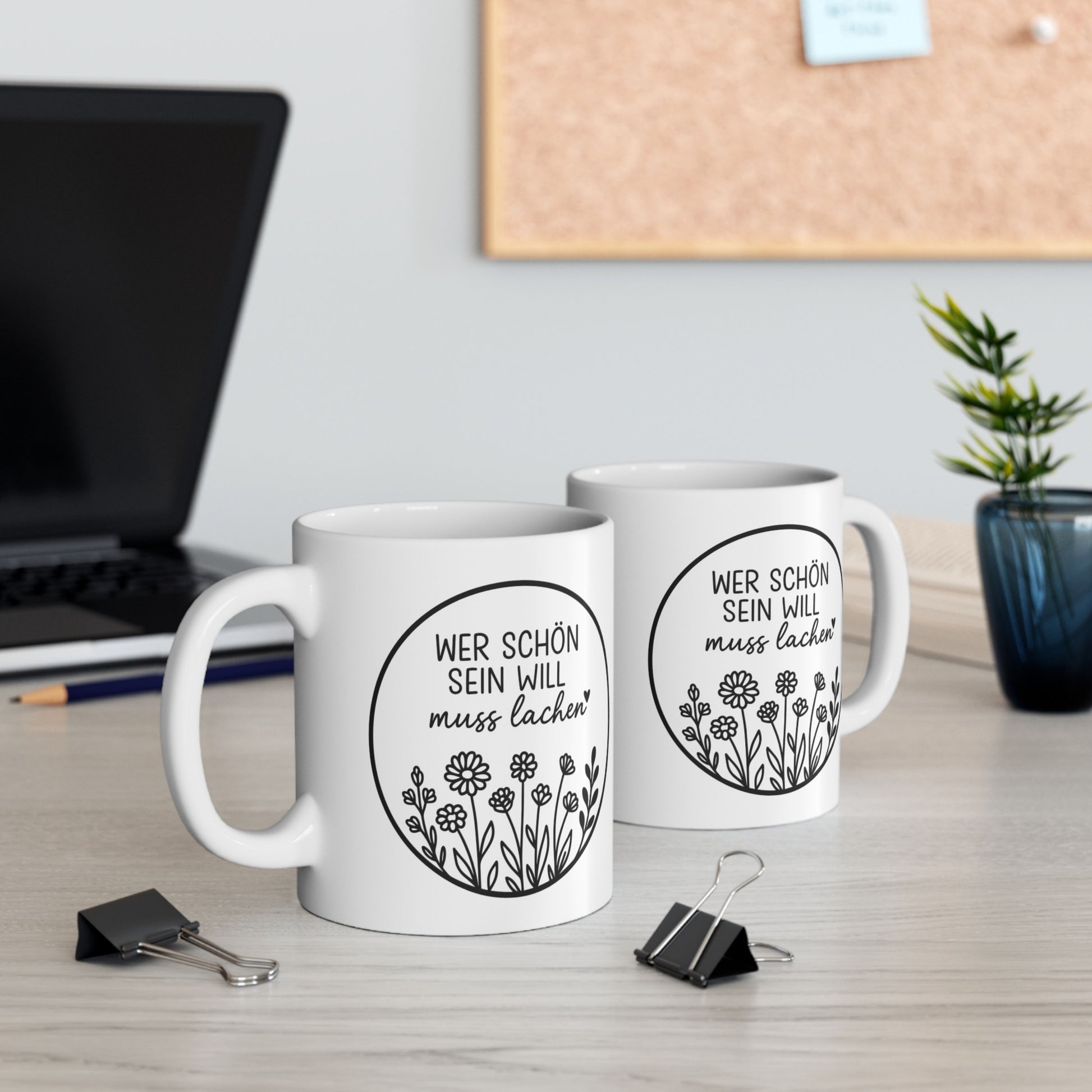 Zwei weiße Tassen mit Spruch Wer schön sein will muss lachen und Blumenmotiv