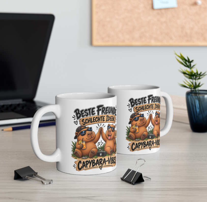 Zwei weiße Capybara Tassen mit Freundschaftsspruch „Beste Freunde, schlechte Ideen“ auf einem Schreibtisch