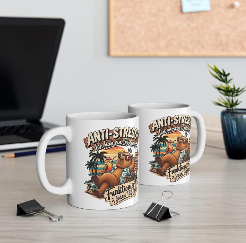 Zwei weiße Capybara Tassen mit Spruch „Anti-Stress? Ich hab ein System!“ und Capybara mit Sonnenbrille auf einem Schreibtisch