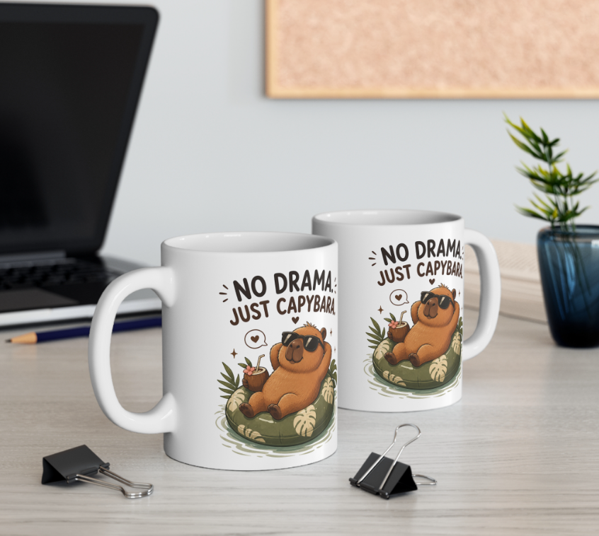Zwei weiße Capybara Tassen mit Spruch „No Drama, Just Capybara“ und entspanntem Capybara mit Sonnenbrille auf einem Schreibtisch